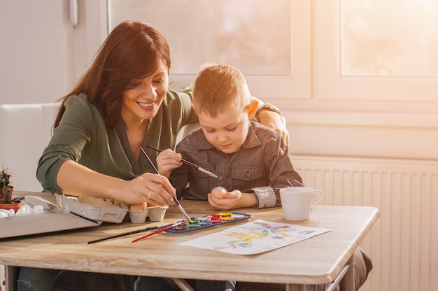 Moeder en zoon die paaseieren schilderen