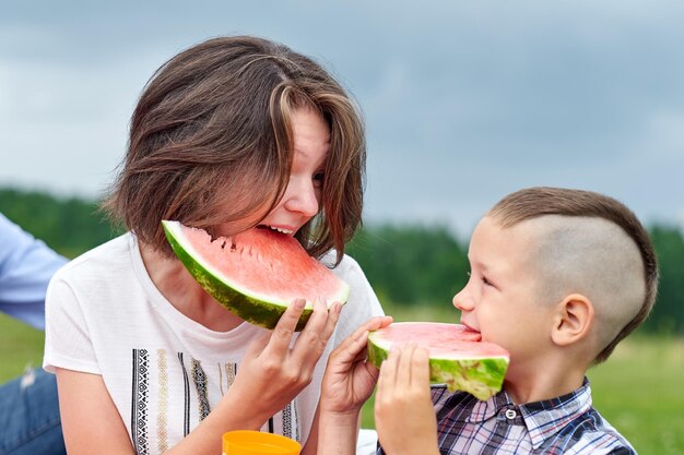 Moeder en zoon die watermeloen eten in weide of park Gelukkig gezin op picknick buitenportret Kleine jongen en moeder