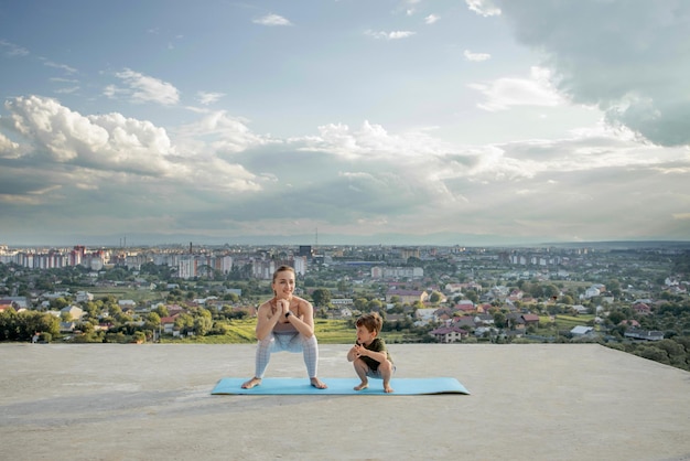 Moeder en zoon doen oefeningen op het balkon op de achtergrond van een stad tijdens zonsopgang of zonsondergang, concept van een gezonde levensstijl.
