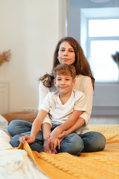 Moeder en zoon glimlachen, knuffelen, hebben plezier, brengen samen tijd door in een ontspannen sfeer thuis terwijl ze zitten