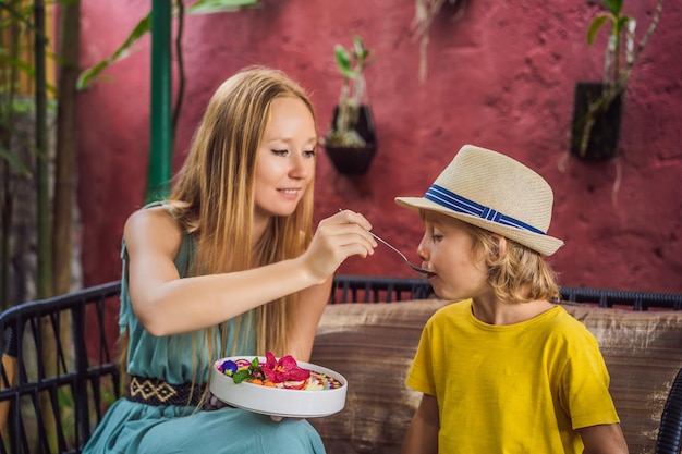 Moeder en zoon hebben een mediterraan ontbijt zittend op de bank en eten gezond tropisch