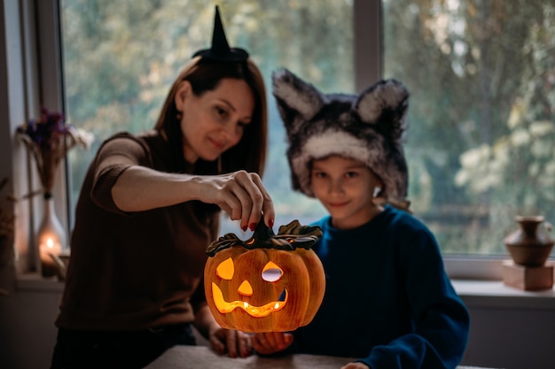 Moeder en zoon in halloweenkostuums spelen thuis samen met jackolantern spookachtige pompoenenlamp