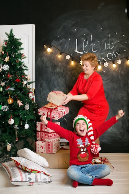 Moeder en zoon in rode kersttruien, plezier hebben bij de kerstboom