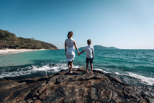 Moeder en zoon kijken samen naar de zee. Moeder houdt de hand van haar kind vast. Achteraanzicht. Zomer zee vakantie concept. Phuket. Thailand