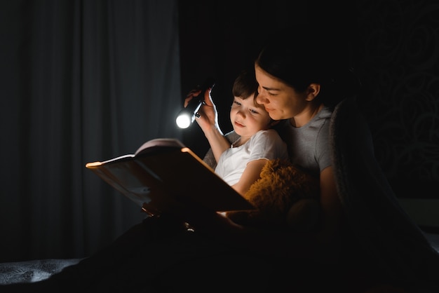 Moeder en zoon lezen van een boek met een zaklamp onder de deken