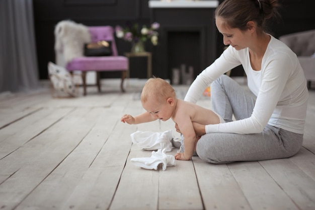 Moeder en zoon liggen 11 maanden samen op de vloer. Moeder verandert kleren voor de baby. De jongen huilt.