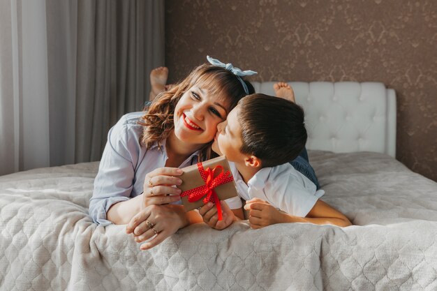 Moeder en zoon liggen op het bed. kind geeft zijn moeder een cadeau voor moederdag.