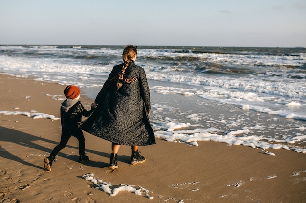 Moeder en zoon lopen op een strand, golven kijken in de winter