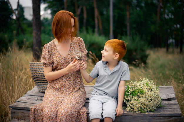 Moeder en zoon met rood haar met een groot boeket wilde bloemen in de natuur in de zomer