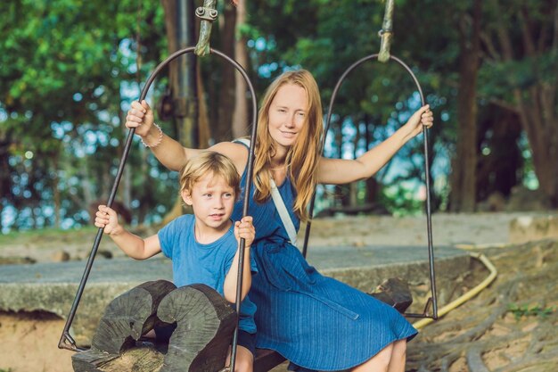 Moeder en zoon slingeren op een oude schommel tegen de achtergrond van de wortels van de boom