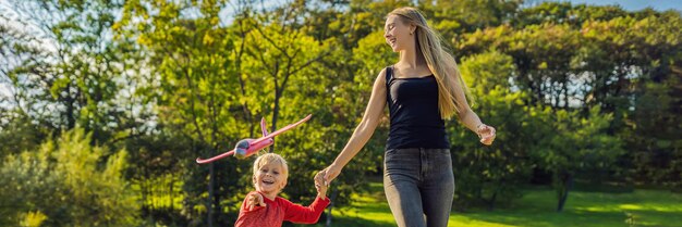 Moeder en zoon spelen met een groot model speelgoedvliegtuig in het park BANNER, LANG FORMAAT