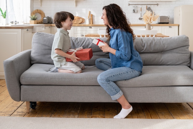 Moeder en zoon vieren samen verjaardag gelukkige moeder en opgewonden zoon zitten op de bank en houden geschenken glimlachend vast