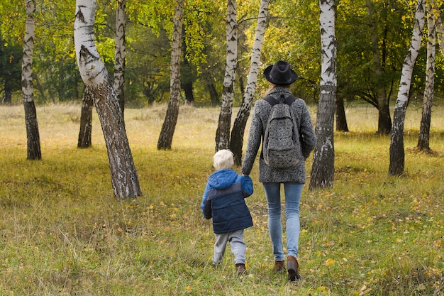 Moeder en zoon wandelen in het bos van de herfst. Uitzicht vanaf de achterkant