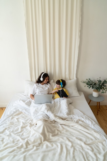 Moeder en zoon werken en studeren samen in bed met laptopcomputer en digitale tablet in de slaapkamer