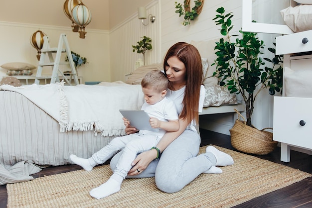 Moeder en zoon zitten op de grond in de kamer en kijken samen naar de digitale tablet