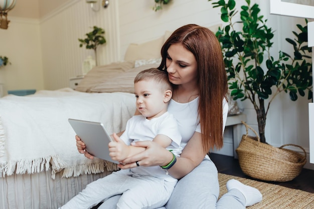 Moeder en zoon zitten op de grond in de kamer en kijken samen naar de digitale tablet