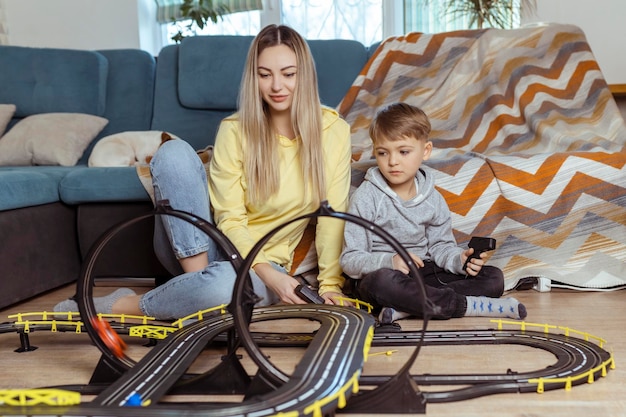 Moeder en zoontje spelen racen op het tapijt thuis veel plezier en knuffel Alleenstaande moeder voedt haar zoon op door auto's te spelen