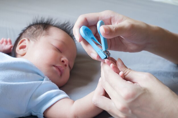 Moeder gebruikt nageltrimmer met babyhand op bed