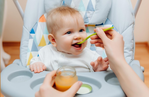 Moeder geeft fruitsaus aan baby moeder voedt baby op kinderstoel babyvoeding