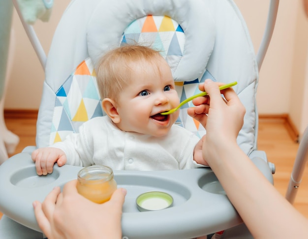 Moeder geeft fruitsaus aan baby moeder voedt baby op kinderstoel babyvoeding