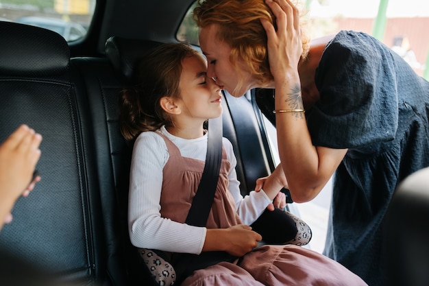 Moeder geeft haar achtjarige dochter een kus. Ze zit op een achterbank in een auto. Vanuit een salon.