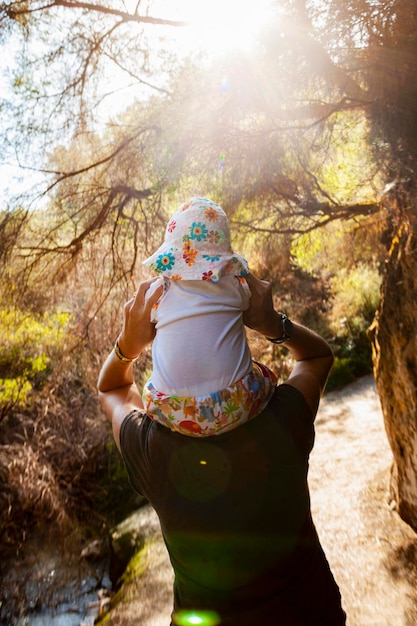 Moeder geeft haar babymeisje een ritje op de rug op het natuurpad bij een thermaal zwembad