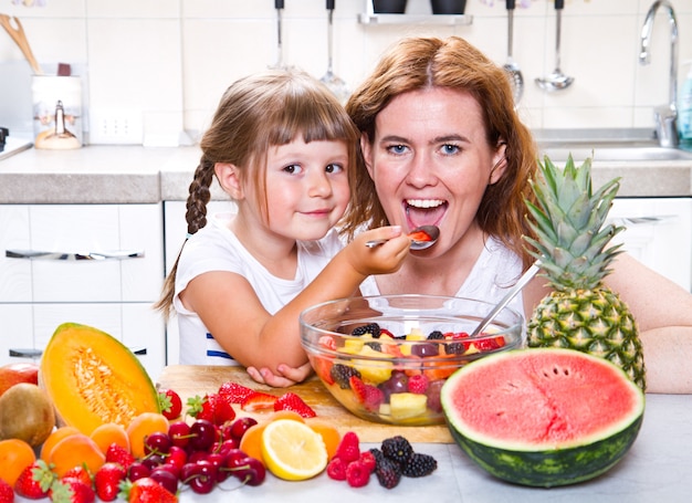 moeder geeft het kleine meisje een fruitsalade in de keuken.