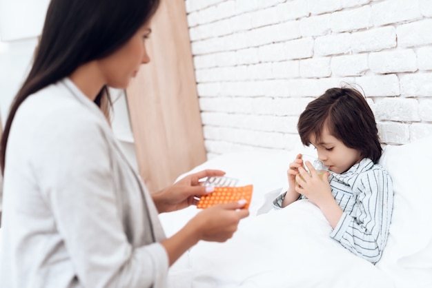 Moeder geeft medicijnen aan een zieke zoon thuis.