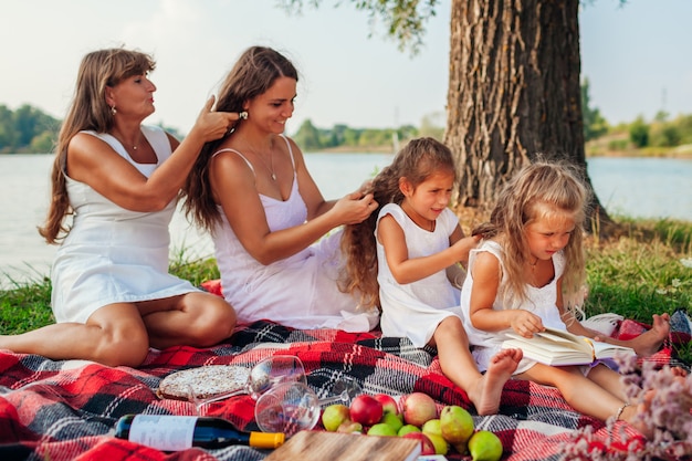 Moeder, grootmoeder en kinderen vlechten elkaar. Familie plezier tijdens picknick in het park. Drie deneraties