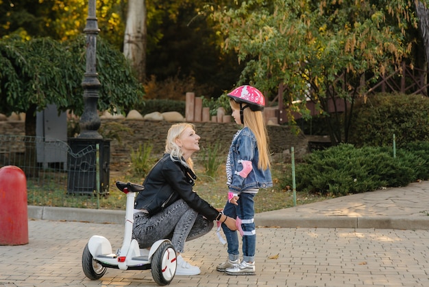 Moeder helpt bij het aankleden van de uitrusting en helm van haar dochtertje voor een Segway-rit in het park