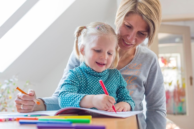 Moeder helpt dochter bij het inkleuren van een boek thuis