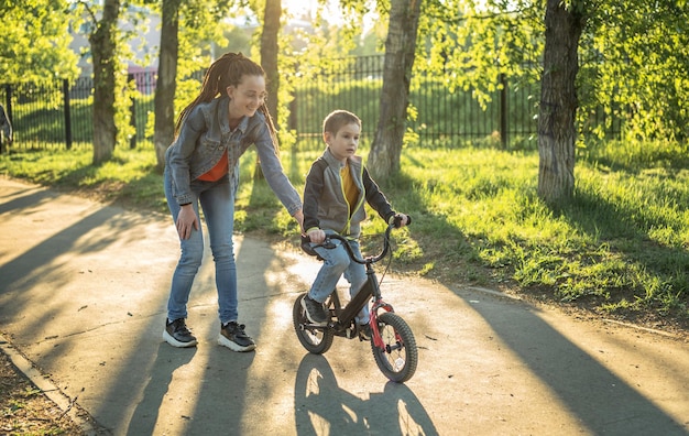 Moeder helpt een jongetje om te leren fietsen op een tweewielige fiets in het park Een plezierige kinderzomersportvakantie