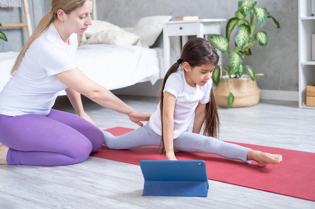 moeder helpt haar dochter om thuis online te stretchen met tablet