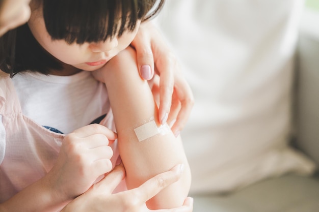 Moeder helpt haar dochter om verband op de wond op haar arm thuis aan te brengen