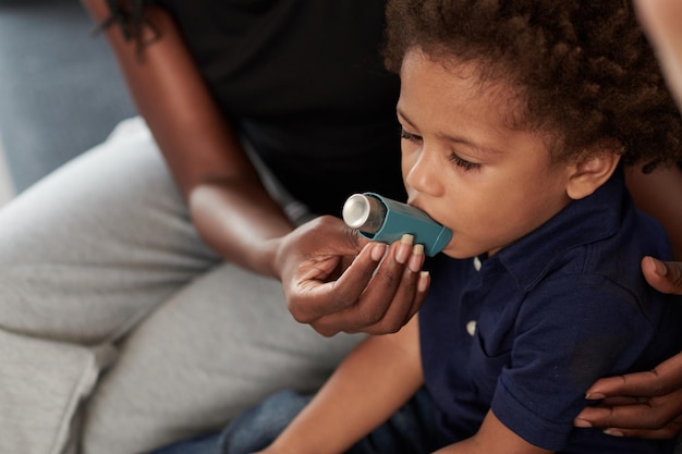 Moeder helpt zoontje om astma-inhalator te gebruiken tegen allergische aanval