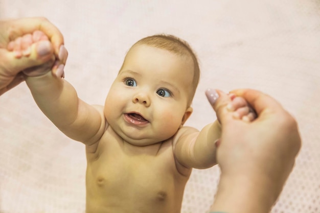 Moeder houdt baby bij de handen en dochter glimlacht tandeloos naar haar