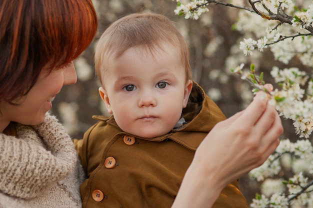 Foto moeder houdt de baby tegen de achtergrond van bloeiende bomen