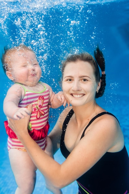 Moeder houdt dochter vast ondergedompeld in water zwemmen onder water in peuterbad Duiken baby Baby leren zwemmen Jonge moeder of zweminstructeur en gelukkig klein meisje