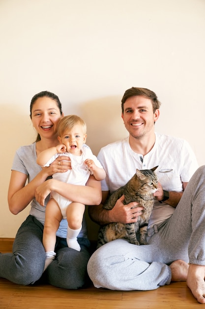 Moeder houdt een klein meisje op schoot en vader houdt een gestreepte kat op schoot