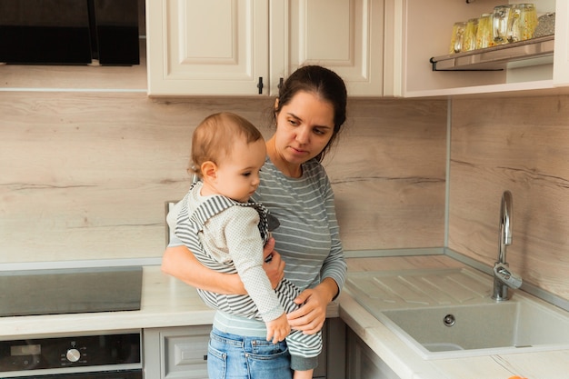 Moeder houdt haar baby in haar armen in de keuken. moeder geeft een appel aan het kind.