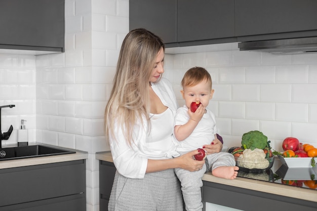 Moeder houdt haar baby vast en eet een appel in de keuken