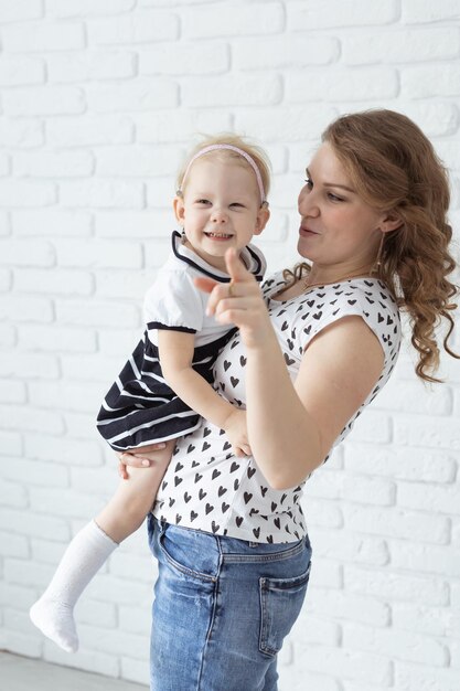 Moeder houdt haar kind met gehoorapparaten en cochleaire implantaten vast op een witte bakstenen muur, doof en gezond