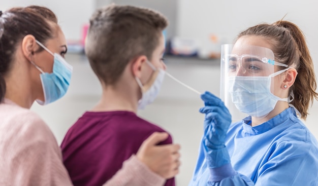 Moeder houdt haar zoon vast terwijl medisch werker een monster uit zijn neus neemt tijdens het testen van een coronaviruspandemie.