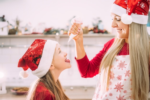 Moeder in een schort en haar tienerdochter vermaken zich in de keuken met kerstmutsen.