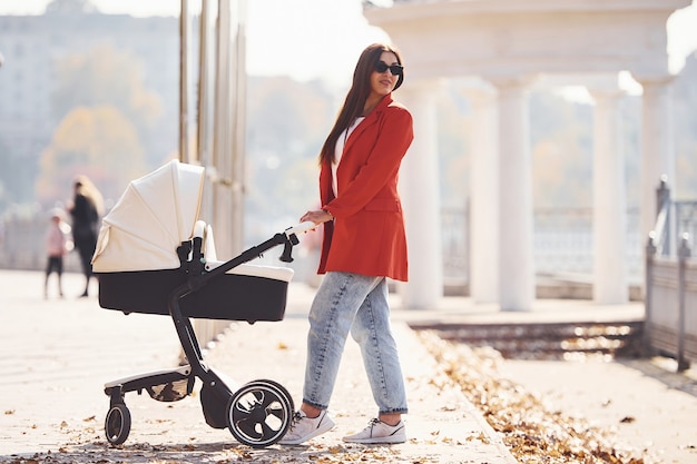 Moeder in rode jas maakt in de herfst een wandeling met haar kind in de kinderwagen in het park.