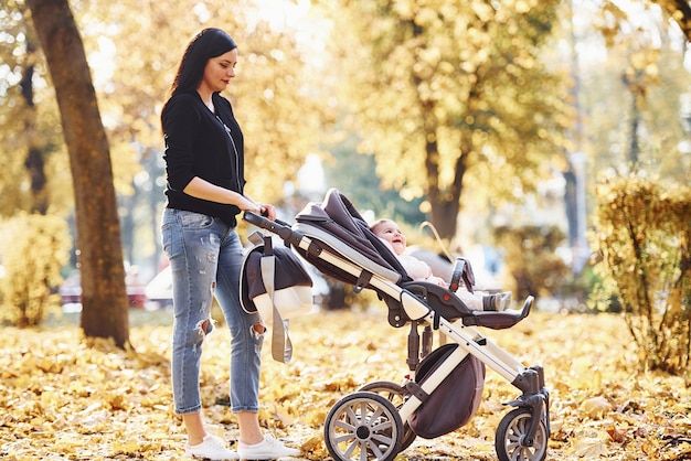 Moeder in vrijetijdskleding met haar kind in kinderwagen is in het prachtige herfstpark.