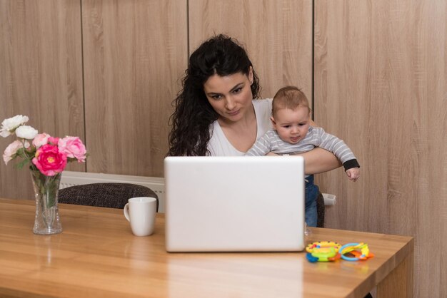 Moeder in woonkamer met baby die laptop gebruikt