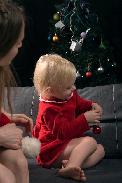 Moeder kijkt toe hoe een klein meisje een kerstboom versiert kerst en oudejaarsavond