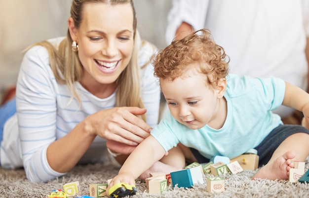 Moeder kind en spelen leren blok speelgoed op de vloer voor educatieve bonding tijd samen in het ouderlijk huis jonge zorgzame en liefhebbende vrouw die peuter helpt met de ontwikkeling en coördinatie van het kind