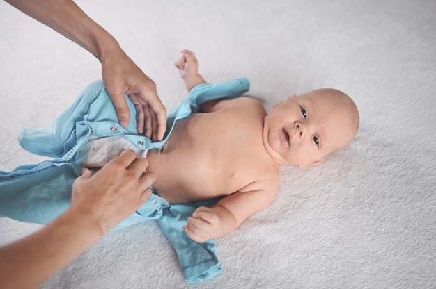 Moeder kleedt schattige emotionele grappige pasgeboren babyjongen in een blauwe jumpsuit Baby baby Nursery